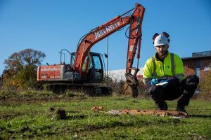 Engineer posing while crouching in front of an excavator